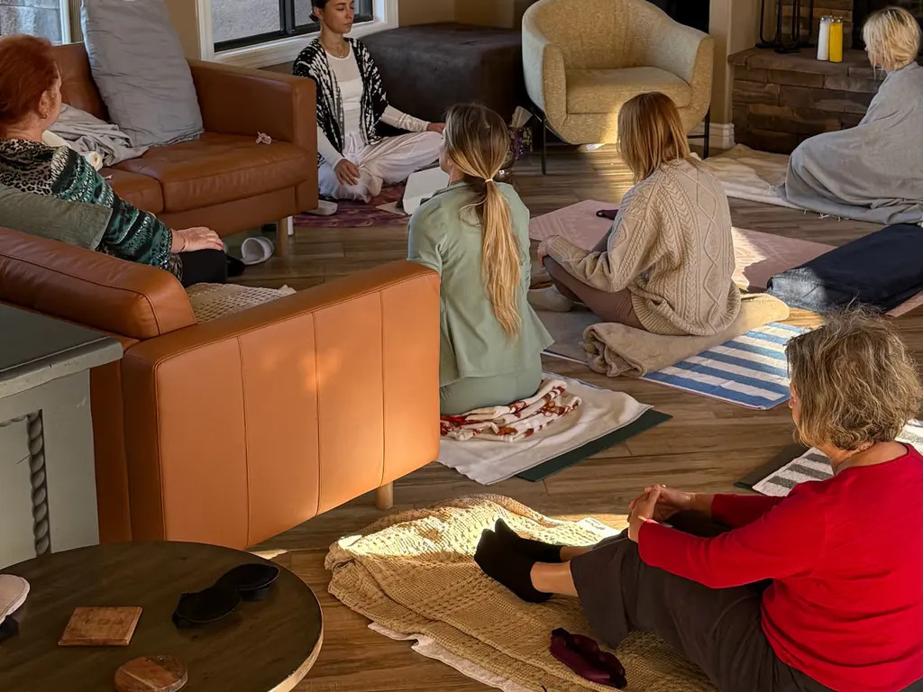 Women sitting on mats in a circle during a group practice in a sunlit room